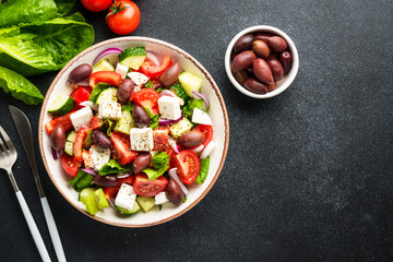 Greek salad in craft plate on black kitchen table. Top view. Vegan food.