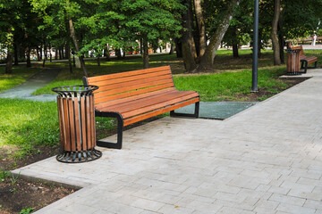 In a serene park, you can find a wellcrafted wooden bench accompanied by a trash can, providing...