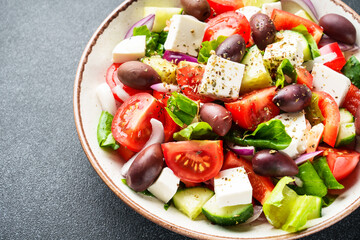 Greek salad in craft plate on black background. Top view. Vegan food, mediterranean diet.