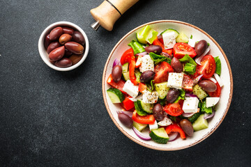 Greek salad in craft plate on black kitchen table. Top view. Vegan food.