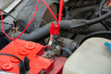 Mechanics conduct battery connection repairs in an automotive engine compartment using multimeter...