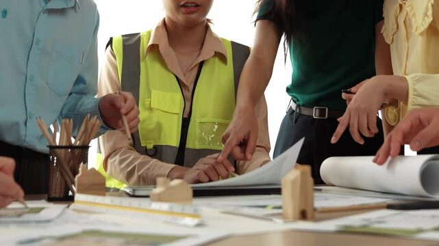 Smart architect and safety engineer discussion about building blueprint on table with architectural document, measurement tools and wooden block scatter around at modern office. Closeup. Delineation.