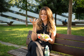 Businesswoman enjoying a healthy lunch break in a park, using her phone