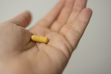 Hand holding single yellow capsule on soft-focused neutral background