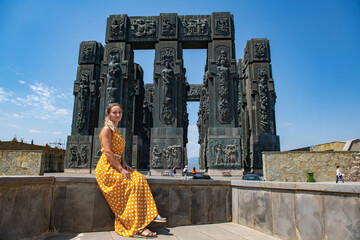 A girl in a yellow dress stands at the monument of the chronicles of Georgia