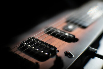Fototapeta premium Close-up shot of a dark brown electric guitar against blurred background, possibly a stage or studio Black neck and headstock, white fret markers, out-of-tune strings Soft shadows cast, shallow dep