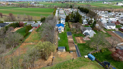 This aerial view captures a quiet suburban neighborhood surrounded by lush green fields. Houses...
