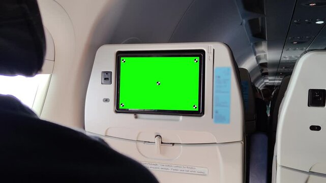 Airplane seatback with green screen monitor for in-flight entertainment, visible USB port, tray table, and part of passenger cabin interior, ideal for chroma key mockup or travel-related media design