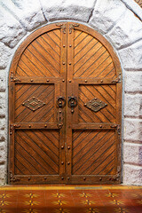 Weathered stone archway with carved wooden doors displaying an interlocking pattern, set in...