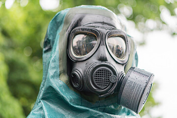 Outdoor shot of a person in full-body green, sealed protective gear, wearing a white gas mask with...