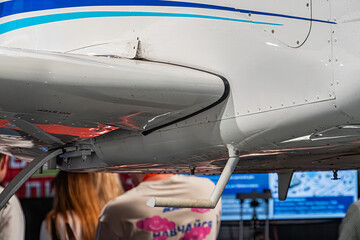 Airplane wing light colored, bluegreen stripes, extended flaps and ailerons, two individuals inspecting, casual clothing, backpack, open area, clear sky, daylight, candid photography