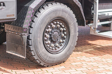 Black tire on rubberized wheel well against light paved ground, parked dark gray vehicle in the...