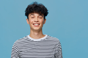 smiling young man with curly hair wearing striped shirt, expressing happiness on blue background in...