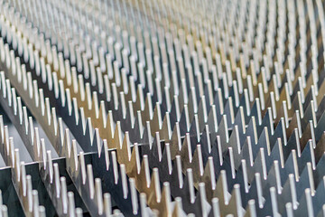 Fototapeta premium Close-up view of a grid of small metal pins on a flat surface, arranged in neat rows and columns, reminiscent of an electronic circuit board or cooling heat sink