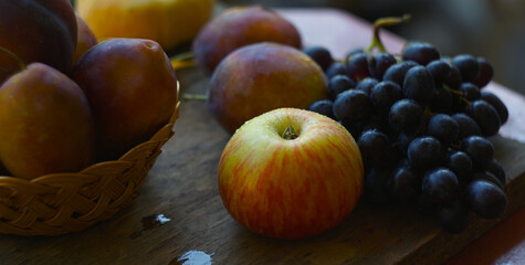 Plums in a basket and various fruits on a wooden table