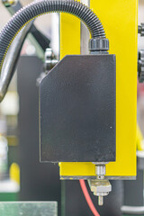 Close-up view of a yellow industrial machine setup, featuring a large dark rectangular component...
