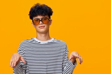 Young man with curly hair wearing large sunglasses and striped shirt poses playfully against a...
