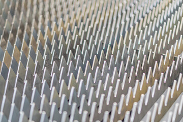 Close-up image of a metal object with uniform, angular spikes, displayed in dull grey tones under direct lighting from above, captured with sharp focus
