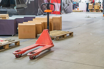 An industrial workshop or factory with a red pallet truck, stacked cardboard boxes, and concrete...