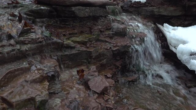 A close-up of a small cascading waterfall flowing over rock strata in the winter.