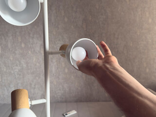 Changing a light bulb in a modern floor lamp at home during daytime