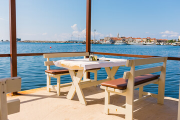 Fototapeta premium Outdoor cafe or restaurant with sea view and empty chairs. Coastal relaxation, summer tourism, and beachfront dining in the Mediterranean region.