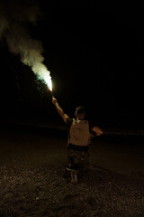 Obraz premium Soldier with his back to the camera wearing army gear holding a flare to be recognized in the darkness