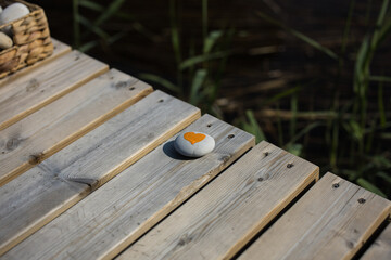 Fototapeta premium Tiny white rock with an orange heart painted on a pier during sunny summer weather
