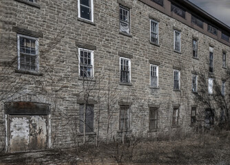 Fototapeta premium Old dilapidated grey stone building with boarded up windows in an overgrown field, nobody