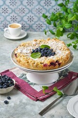 Shortcrust pie with custard filling and fresh honeysuckle or blueberries on a cake stand on a grey concrete background. Berry desserts.