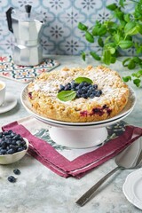 Shortcrust pie with custard filling and fresh honeysuckle or blueberries on a cake stand on a grey concrete background. Berry desserts.