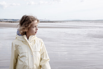 Thoughtful Child Gazing on Broad Beach. Pensive Child on Expansive Pembrokeshire Beach. A young...