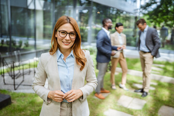 confident woman smiles in suit stand in front of modern glass building