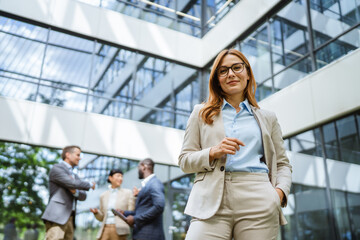 confident woman smiles in suit stand in front of modern glass building
