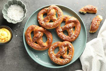Tasty pretzels with salt and sauce on grey table, flat lay