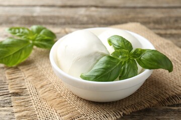 Tasty mozzarella cheese and basil on wooden table, closeup