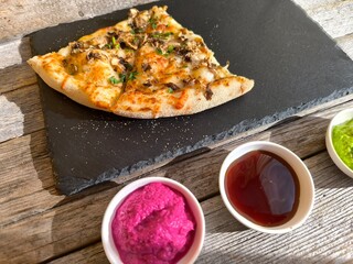 delicious slice of pizza lies on a black granite board. Various sauces are nearby