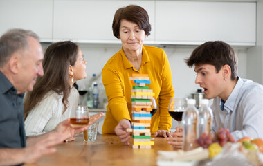 Smiling adult woman or Mother having fun enjoying tower building game with husband and adult children at light comfortable family home