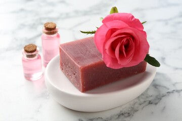 Soap bars, cosmetic products and beautiful rose on white marble table, closeup