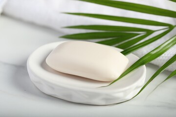 Soap bar, towel and palm leaf on white marble table, closeup