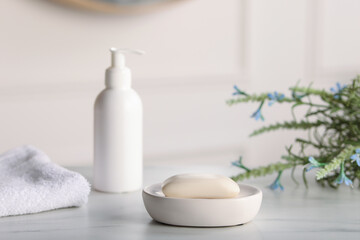 Soap bar, bottle of cosmetic product, towel and flowers on white marble table, closeup