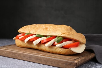 Tasty sandwich with mozzarella cheese, tomatoes and basil on grey textured table against dark background, closeup