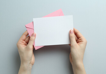 Fototapeta premium Woman holding envelope with blank invitation card on grey background, top view. Space for design