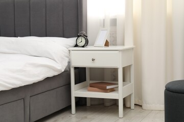 Bedside table with alarm clock and frame near bed indoors
