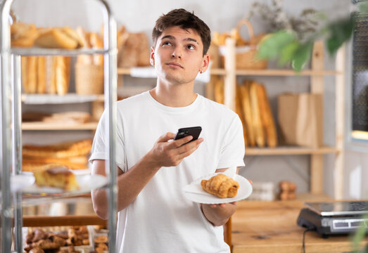 Male customer takes photo of tasty croissant using smartphone in interior of a private bakery