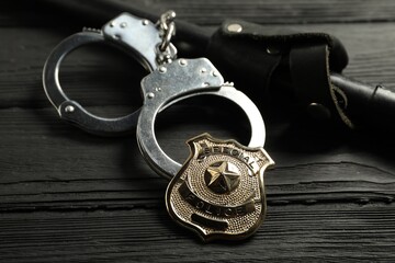 Police badge, handcuffs and baton on black wooden table, closeup