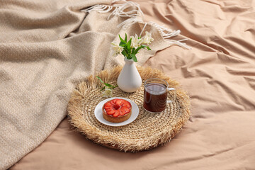 Tray with delicious breakfast and flowers on bed indoors