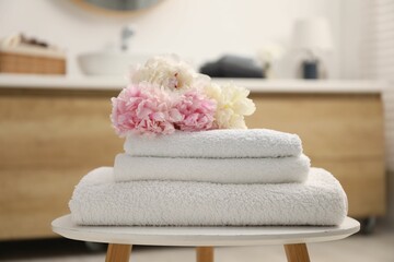 Stack of soft towels and peony flowers on table in bathroom © New Africa
