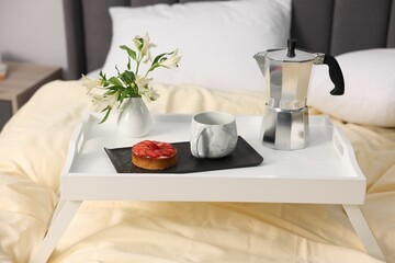 Tray with delicious breakfast and flowers on bed indoors