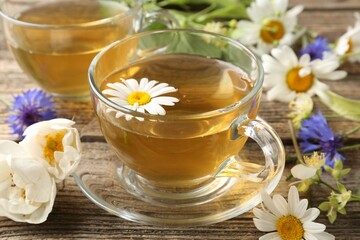 Aromatic herbal tea in glass cups and flowers on wooden table, closeup